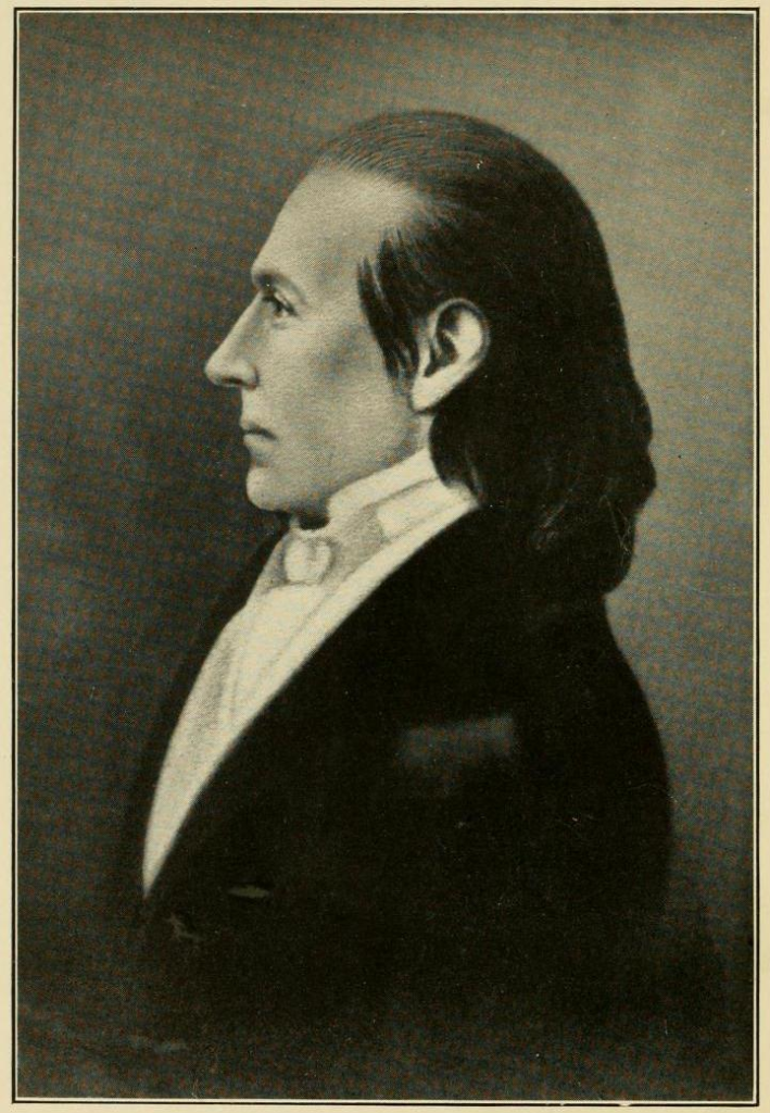 Yellow tinted photograph of William Graham. Shows his side profile; long dark hair, widow's peak, black jacket.