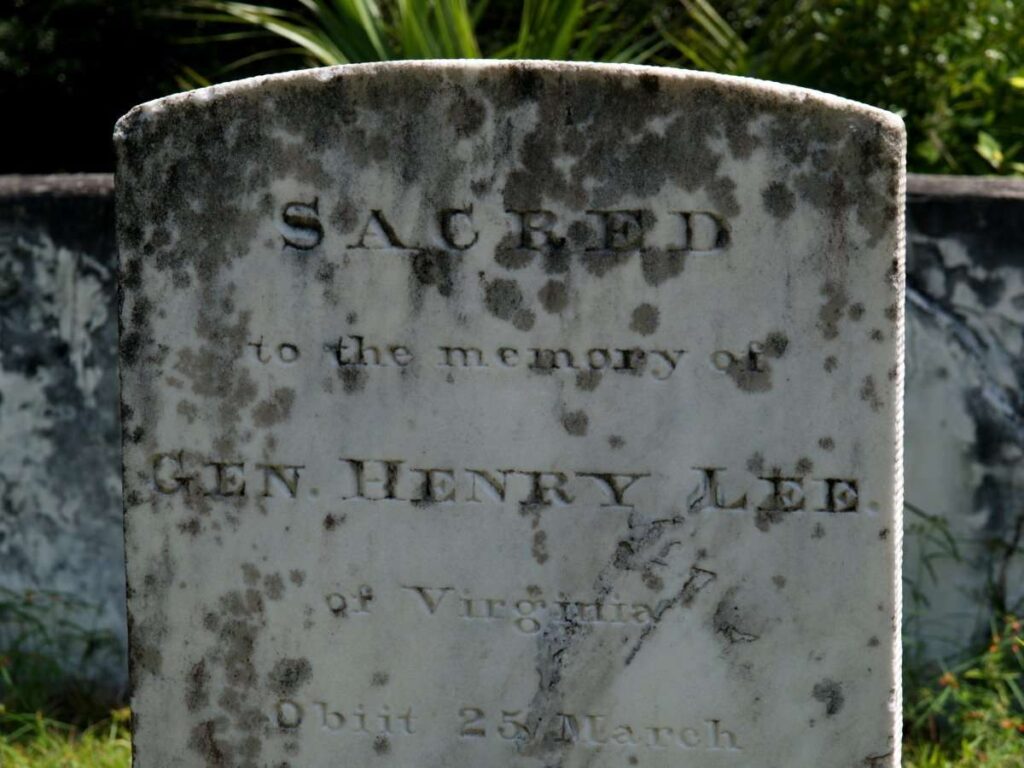 Modern color photograph of Harry Lee's first gravestone. Stone is light grey with dark moss on the top.